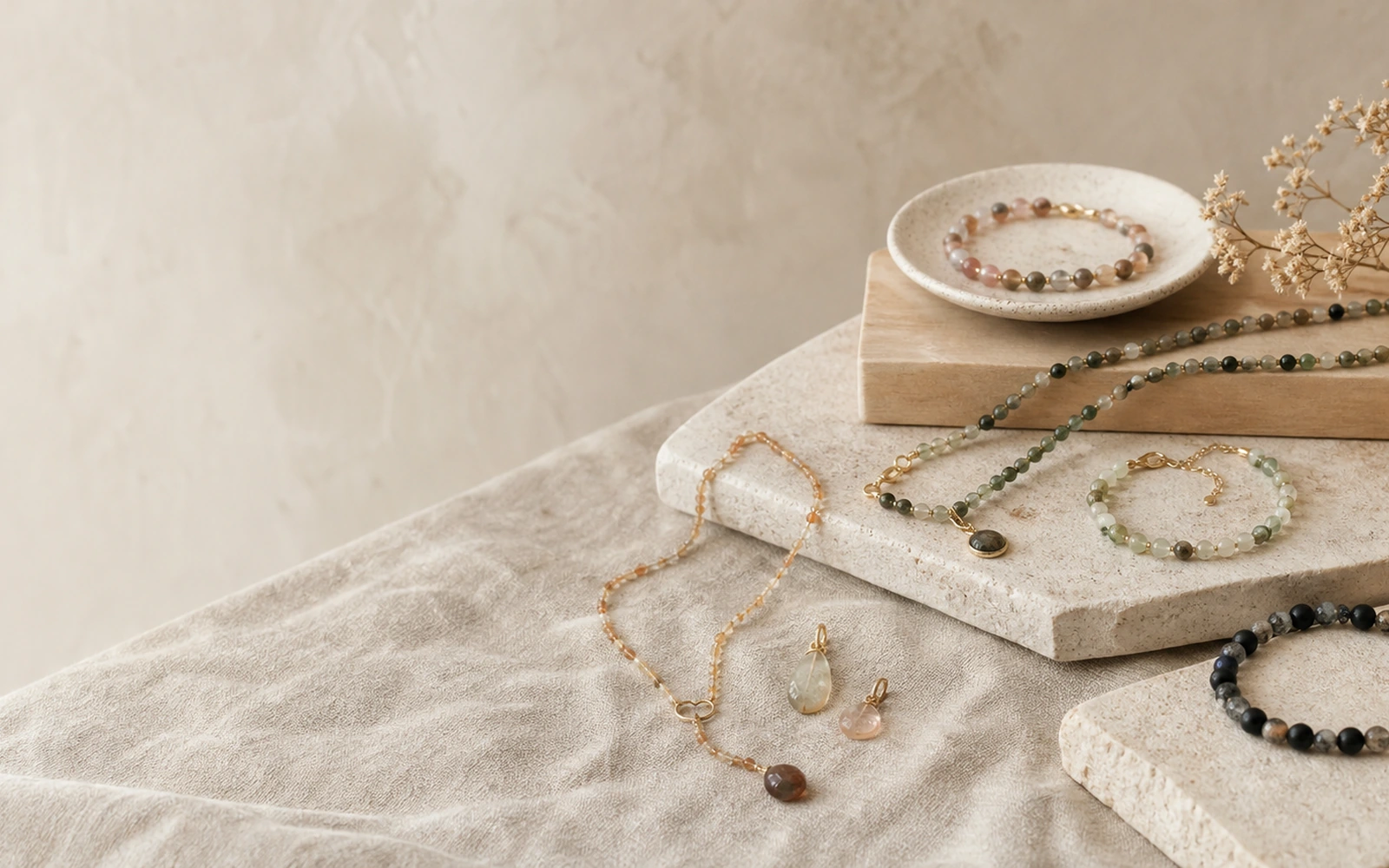 Handmade natural stone jewelry arranged across warm stone and textile surfaces