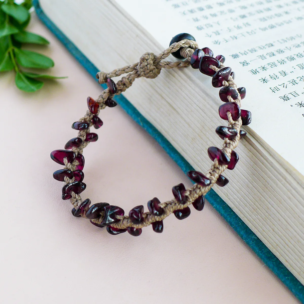 Adjustable garnet chip macrame bracelet with sliding closure styled on a book