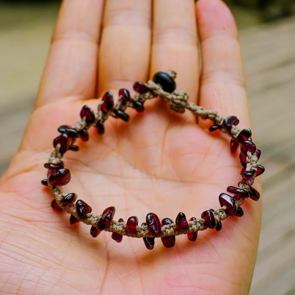 Hand holding an adjustable natural garnet chip macrame bracelet to show scale