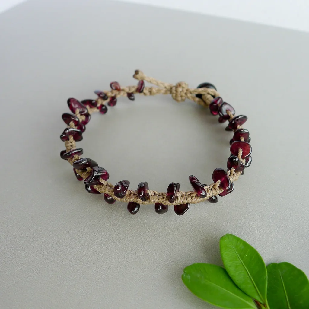 Natural garnet chip bracelet with brown waxed cord styled beside green leaves