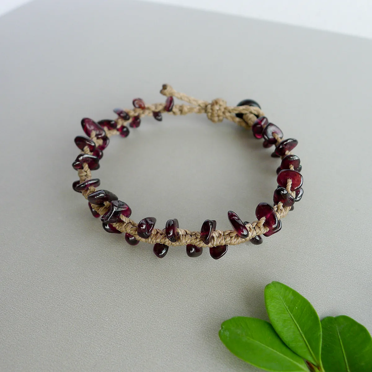 Natural garnet chip bracelet with brown waxed cord styled beside green leaves