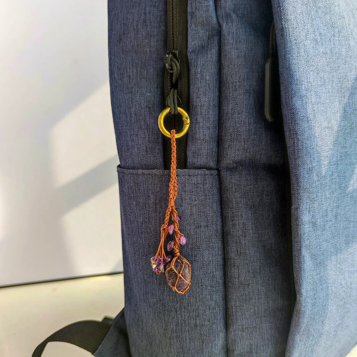 Violet Thread raw amethyst keychain used as a bag charm clipped to a dark backpack zipper. Demonstrates use as a backpack accessory.