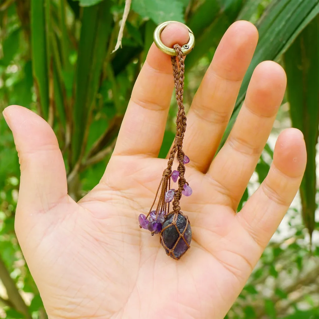 Violet Thread raw amethyst keychain resting in an open palm to show scale. Demonstrates the small wearable size of the macrame and amethyst piece.