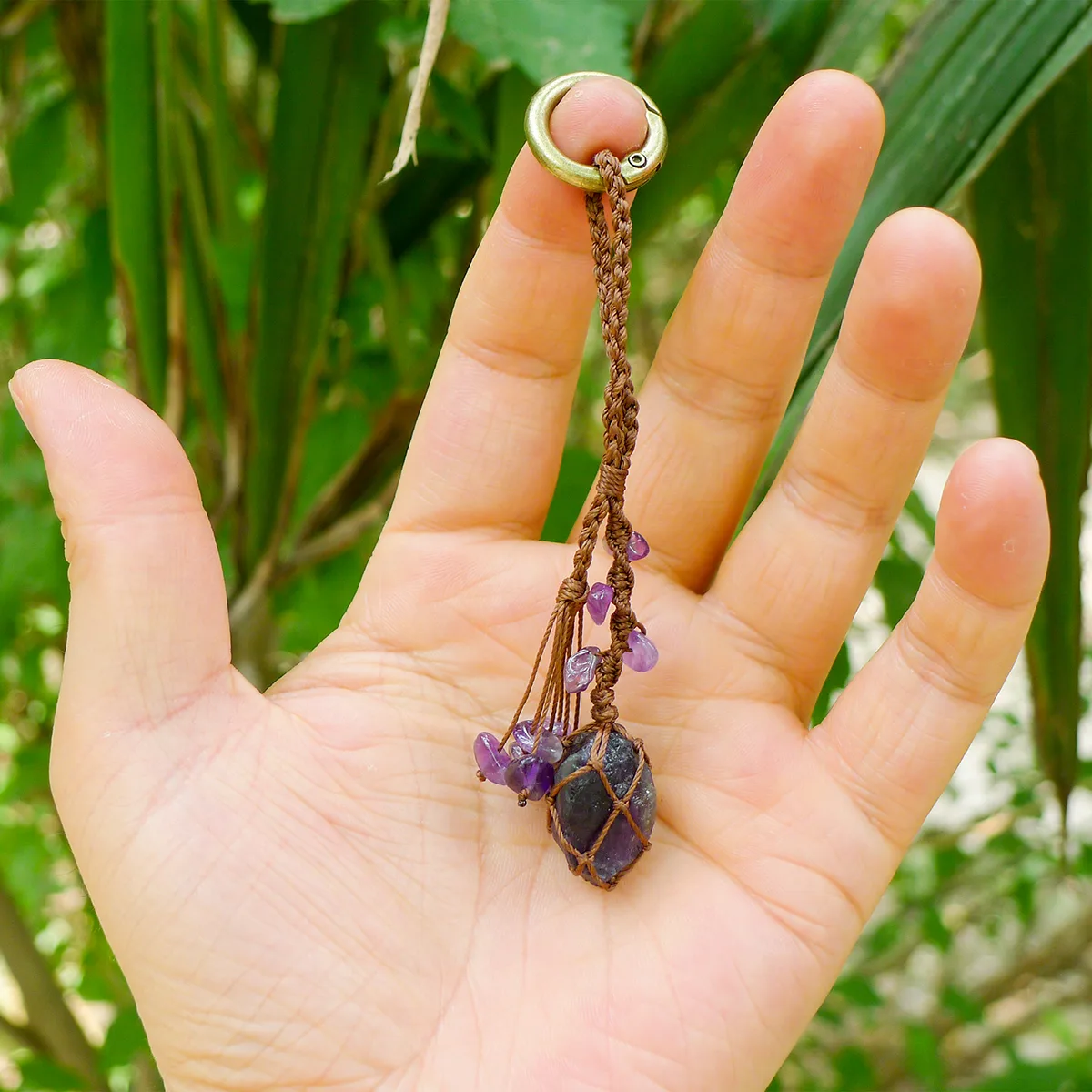 Violet Thread raw amethyst keychain resting in an open palm to show scale. Demonstrates the small wearable size of the macrame and amethyst piece.