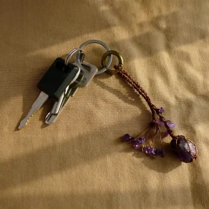 Violet Thread raw amethyst keychain clipped onto a keyring next to other everyday keys on tan fabric. Shows practical use as a keychain accessory.