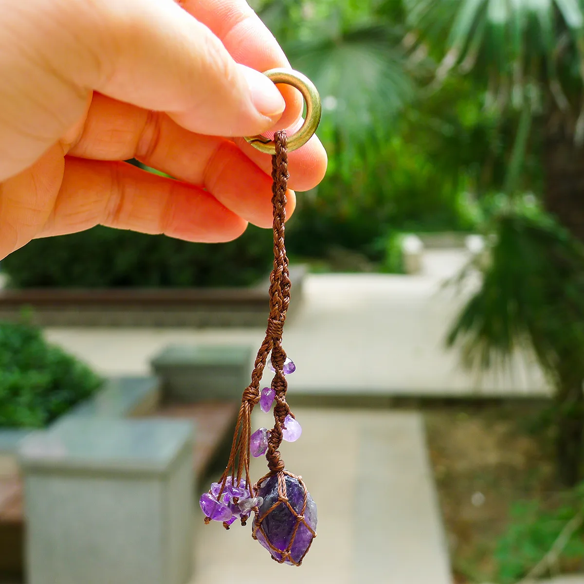 Violet Thread raw amethyst keychain held in a hand against a green plant background. Highlights the spring ring clasp attachment mechanism.